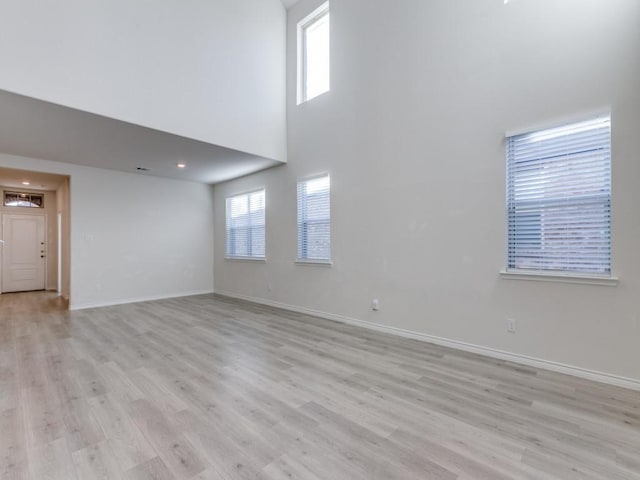 unfurnished living room featuring a high ceiling and light hardwood / wood-style flooring