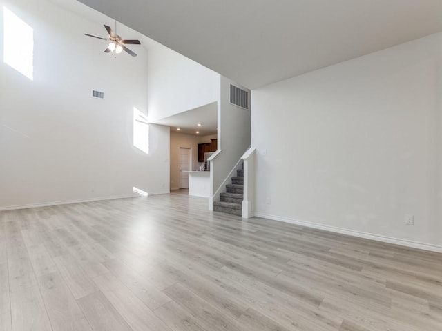 unfurnished living room with ceiling fan, a towering ceiling, and light wood-type flooring