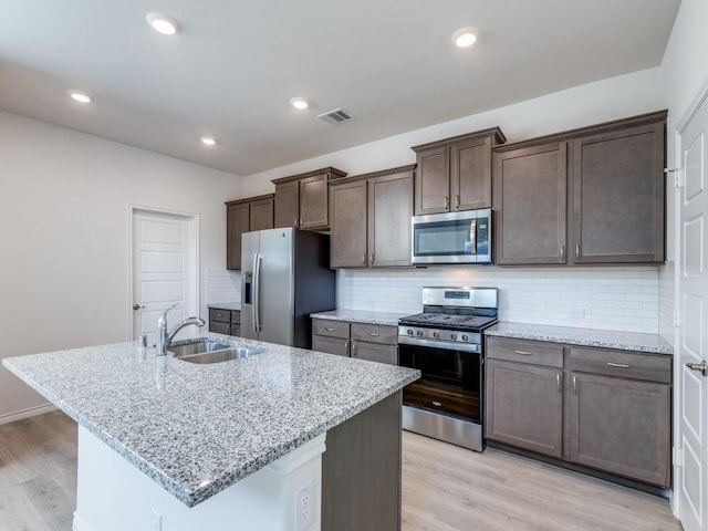 kitchen featuring light stone countertops, sink, stainless steel appliances, light hardwood / wood-style flooring, and a center island with sink