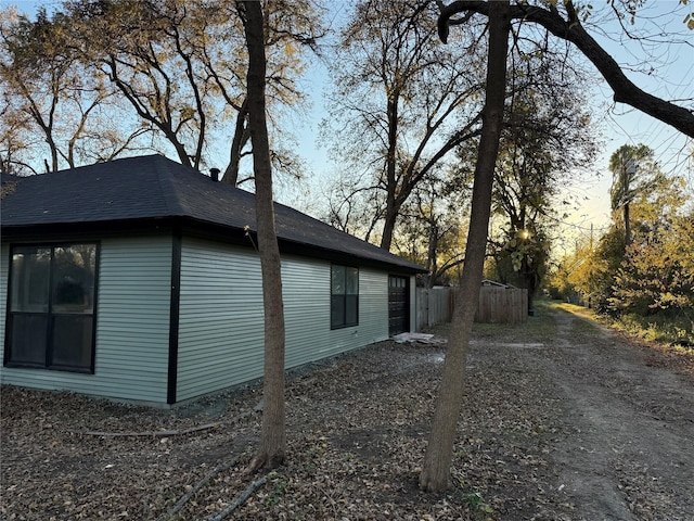 view of side of home featuring roof with shingles and fence