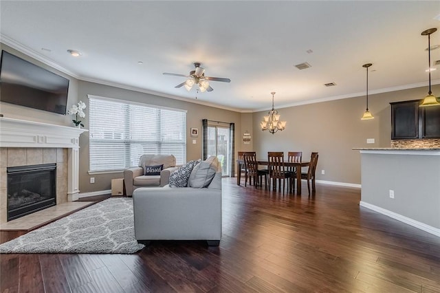 living room featuring a tile fireplace, ceiling fan with notable chandelier, dark wood-type flooring, and ornamental molding