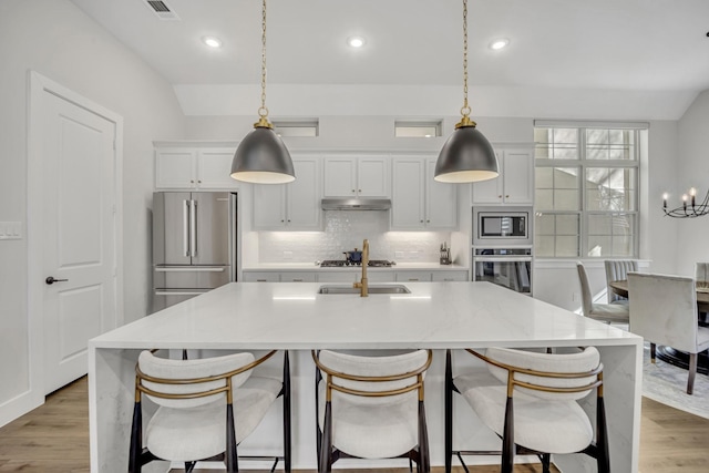 kitchen with a center island with sink, appliances with stainless steel finishes, pendant lighting, light stone counters, and white cabinets