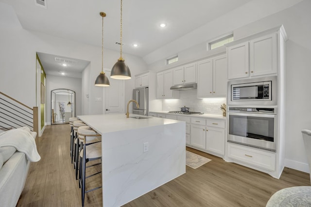 kitchen with white cabinets, stainless steel appliances, decorative light fixtures, and a center island with sink