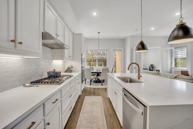 kitchen with appliances with stainless steel finishes, an island with sink, white cabinets, decorative light fixtures, and sink