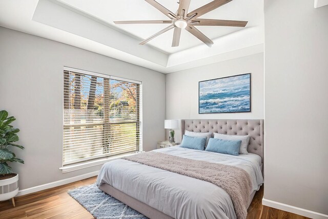 bedroom featuring ceiling fan, a raised ceiling, multiple windows, and hardwood / wood-style flooring