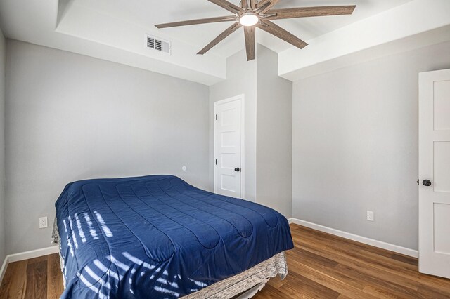 bedroom featuring ceiling fan, hardwood / wood-style floors, and a raised ceiling