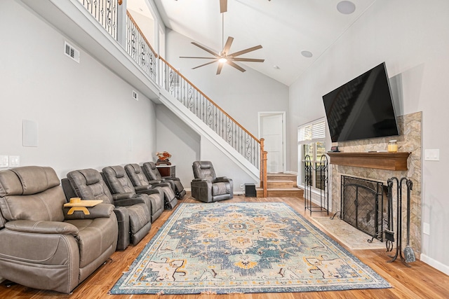 living room featuring hardwood / wood-style flooring, high vaulted ceiling, ceiling fan, and a stone fireplace