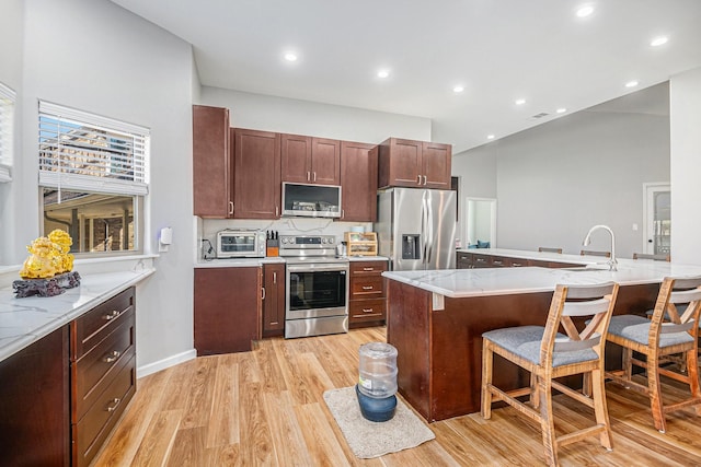 kitchen with stainless steel appliances, light hardwood / wood-style floors, a breakfast bar, and light stone countertops