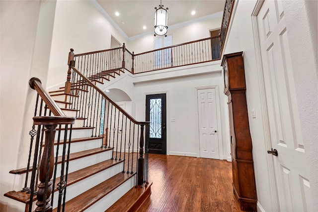 entryway with a towering ceiling, dark wood-type flooring, and ornamental molding