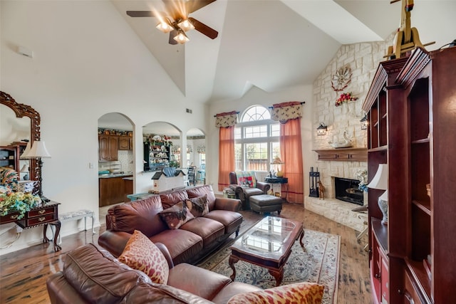 living room featuring hardwood / wood-style floors, ceiling fan, a stone fireplace, and high vaulted ceiling