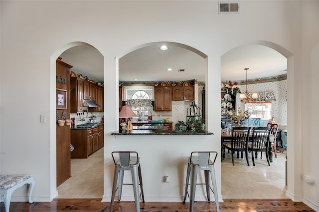 kitchen with decorative backsplash, stainless steel gas stovetop, light tile patterned floors, a notable chandelier, and hanging light fixtures