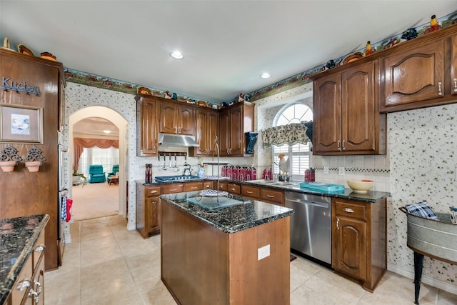 kitchen with light tile patterned floors, stainless steel appliances, a kitchen island, and dark stone countertops