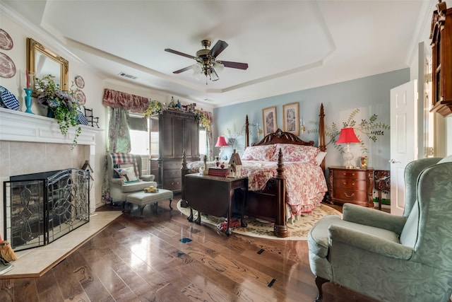 bedroom featuring hardwood / wood-style flooring, ceiling fan, a raised ceiling, and a tile fireplace