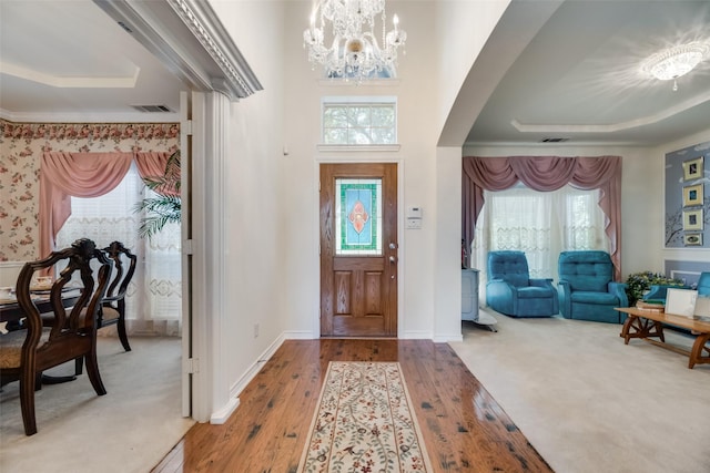 carpeted foyer with a raised ceiling, plenty of natural light, and an inviting chandelier