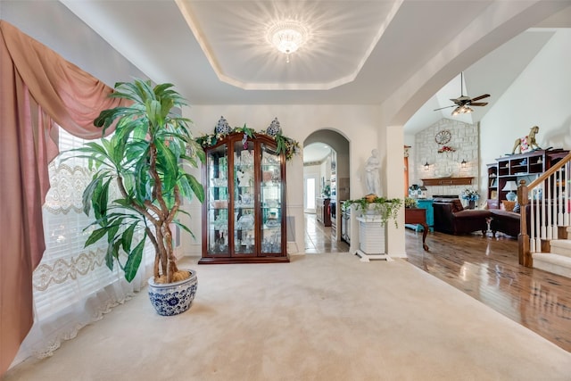 entryway with a fireplace, carpet, a raised ceiling, and ceiling fan