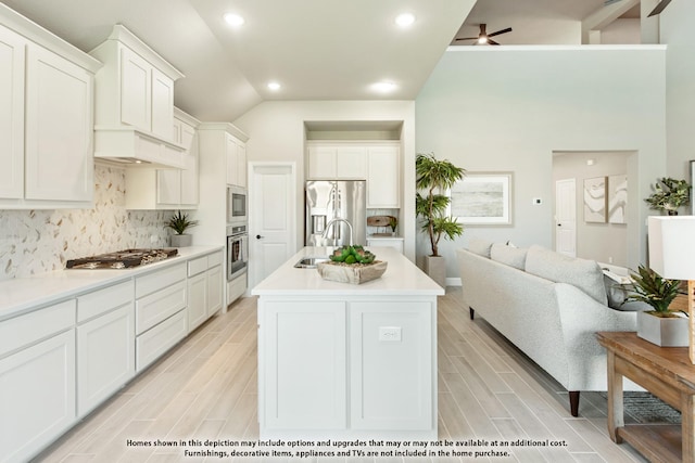 kitchen featuring tasteful backsplash, stainless steel appliances, a kitchen island with sink, white cabinetry, and lofted ceiling