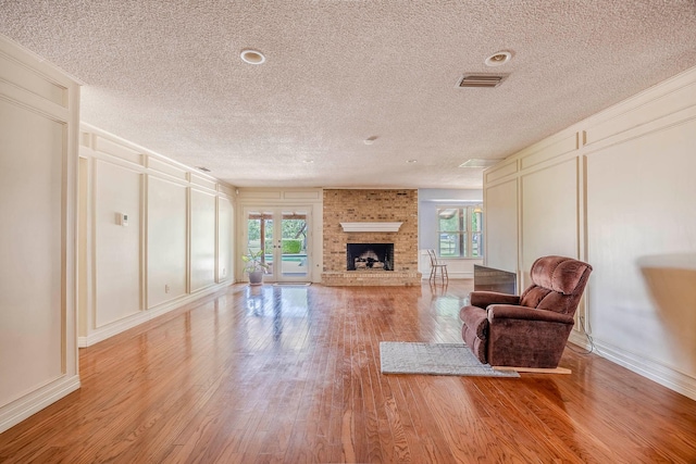 living room with light hardwood / wood-style floors, a textured ceiling, and a brick fireplace