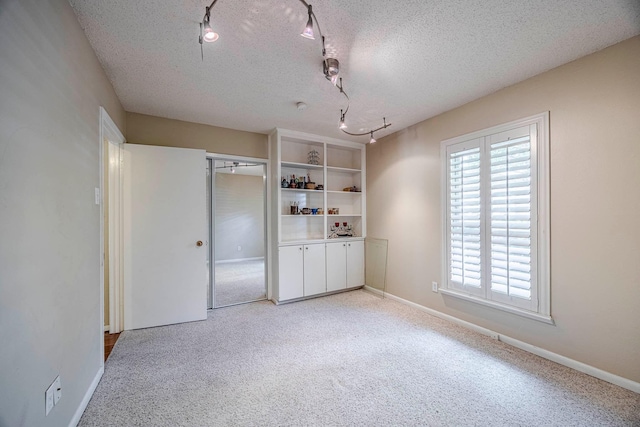 unfurnished bedroom featuring a textured ceiling, a closet, light carpet, and track lighting