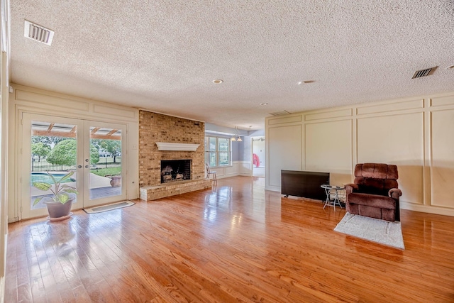 living room with french doors, light hardwood / wood-style floors, plenty of natural light, and a brick fireplace