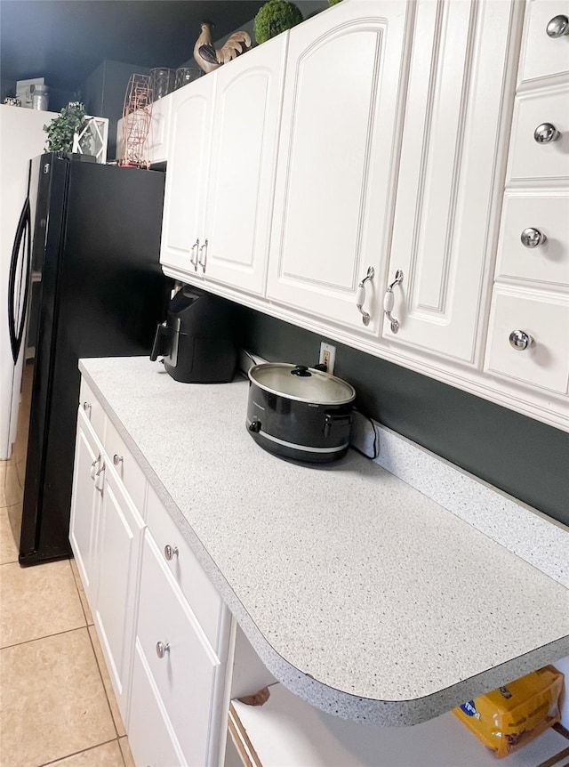 kitchen featuring white cabinets, light tile patterned floors, and black fridge