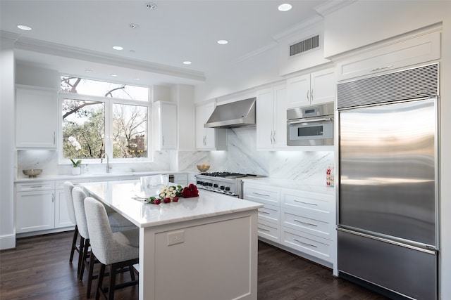 kitchen featuring a center island, wall chimney exhaust hood, decorative backsplash, high quality appliances, and white cabinets