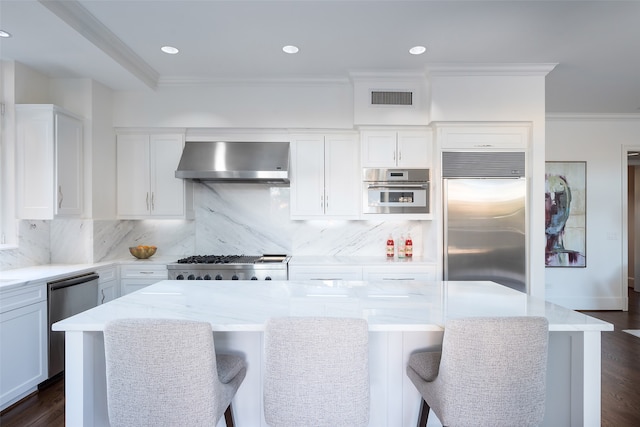 kitchen with white cabinetry, wall chimney range hood, a breakfast bar area, and appliances with stainless steel finishes