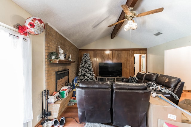 living room with a brick fireplace, a textured ceiling, ceiling fan, lofted ceiling with beams, and hardwood / wood-style floors