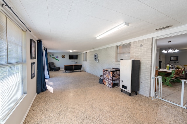 basement featuring an inviting chandelier, ornamental molding, and brick wall