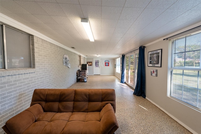 living room featuring crown molding, a healthy amount of sunlight, and brick wall