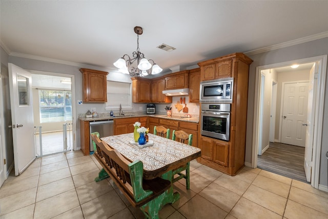 kitchen featuring sink, hanging light fixtures, ornamental molding, appliances with stainless steel finishes, and a chandelier