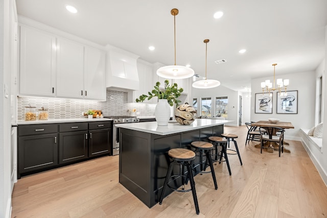 kitchen with a center island, white cabinetry, hanging light fixtures, light hardwood / wood-style flooring, and gas stove