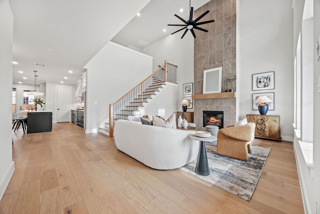 living room featuring ceiling fan, a high ceiling, light hardwood / wood-style flooring, and a fireplace