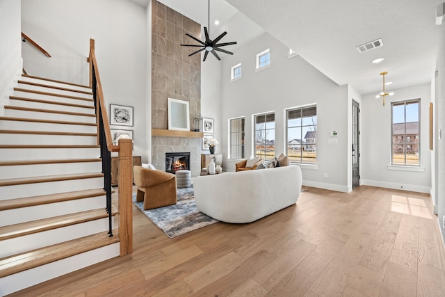 living room featuring ceiling fan with notable chandelier, a high ceiling, light hardwood / wood-style flooring, and a fireplace