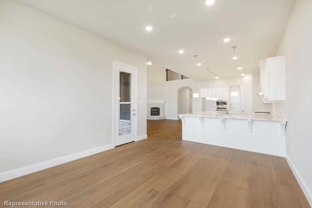 kitchen with kitchen peninsula, light wood-type flooring, decorative light fixtures, white cabinetry, and a breakfast bar area