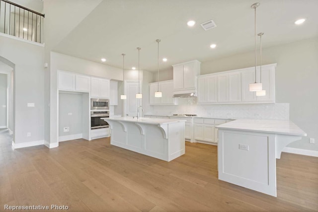 kitchen featuring white cabinets, a kitchen bar, a center island with sink, and appliances with stainless steel finishes