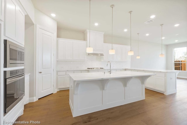 kitchen featuring light hardwood / wood-style flooring, white cabinets, an island with sink, and appliances with stainless steel finishes