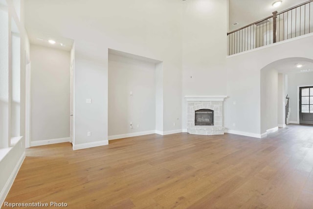 unfurnished living room with a fireplace, a towering ceiling, and light hardwood / wood-style floors