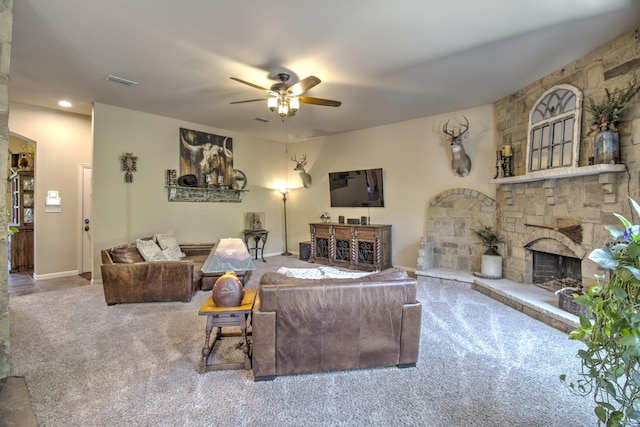 living room featuring ceiling fan, a stone fireplace, and carpet flooring