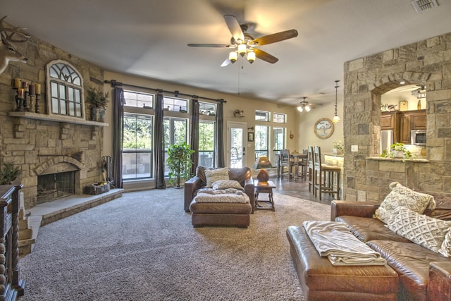 carpeted living room featuring ceiling fan and a stone fireplace