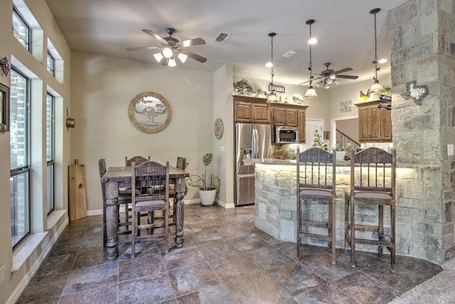 kitchen with ceiling fan, pendant lighting, stainless steel appliances, light stone counters, and a breakfast bar area