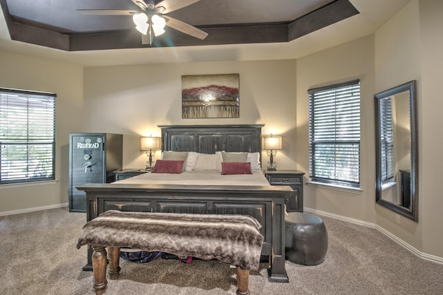 carpeted bedroom with ceiling fan and a tray ceiling