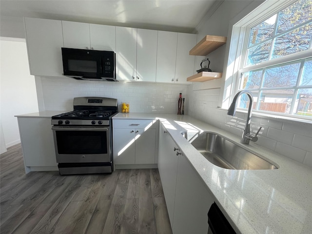 kitchen featuring stainless steel gas range oven, light stone counters, sink, and white cabinets