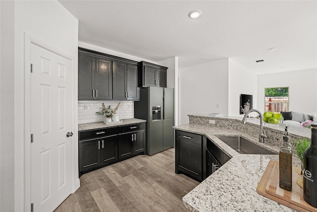 kitchen with light stone countertops, sink, tasteful backsplash, stainless steel fridge with ice dispenser, and light hardwood / wood-style floors