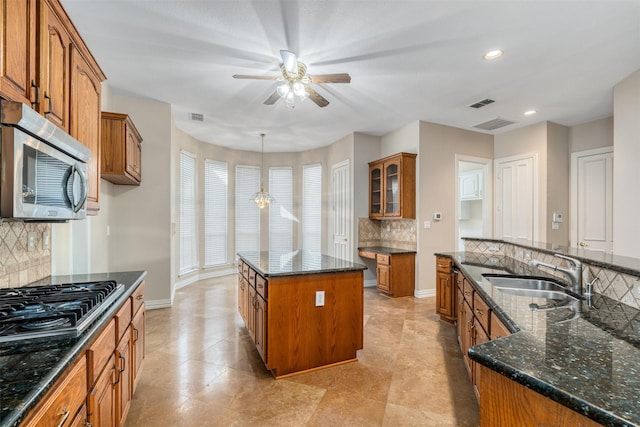 kitchen with appliances with stainless steel finishes, dark stone counters, backsplash, and a center island with sink