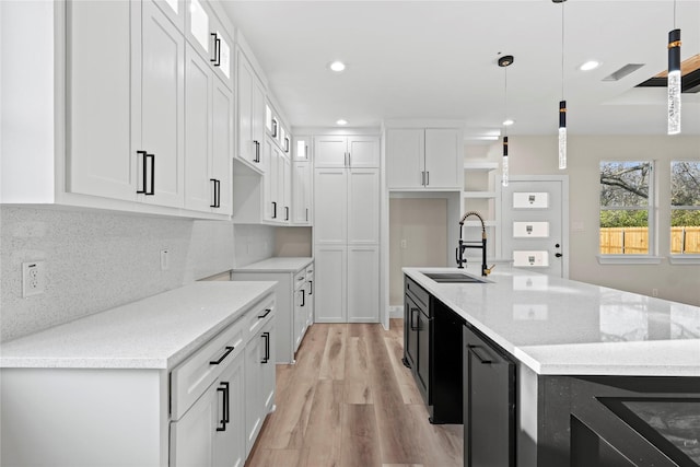 kitchen with pendant lighting, white cabinetry, sink, backsplash, and light stone countertops