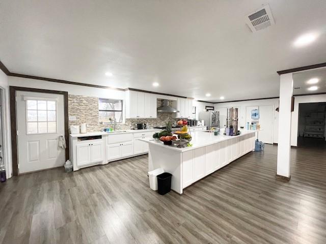 kitchen featuring a center island, white cabinets, wall chimney range hood, sink, and stainless steel fridge