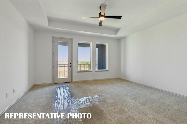 empty room with ceiling fan, light carpet, and a tray ceiling