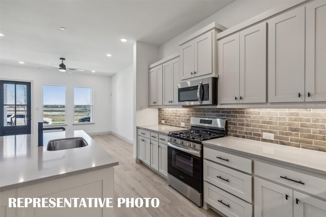 kitchen featuring ceiling fan, sink, stainless steel appliances, light hardwood / wood-style floors, and decorative backsplash