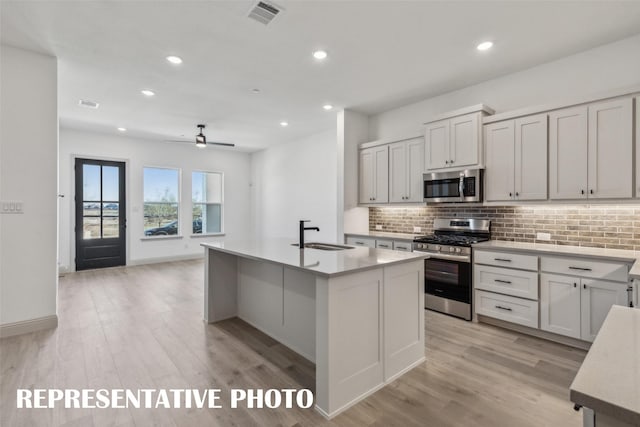 kitchen with ceiling fan, sink, a kitchen island with sink, stainless steel appliances, and decorative backsplash