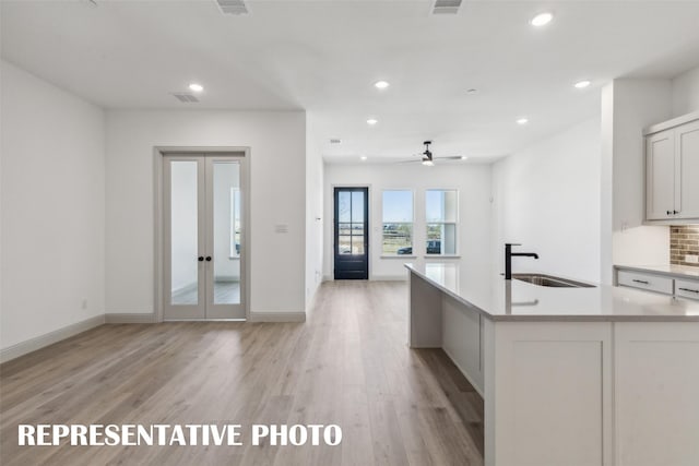 kitchen with a kitchen island with sink, french doors, white cabinets, sink, and light hardwood / wood-style floors